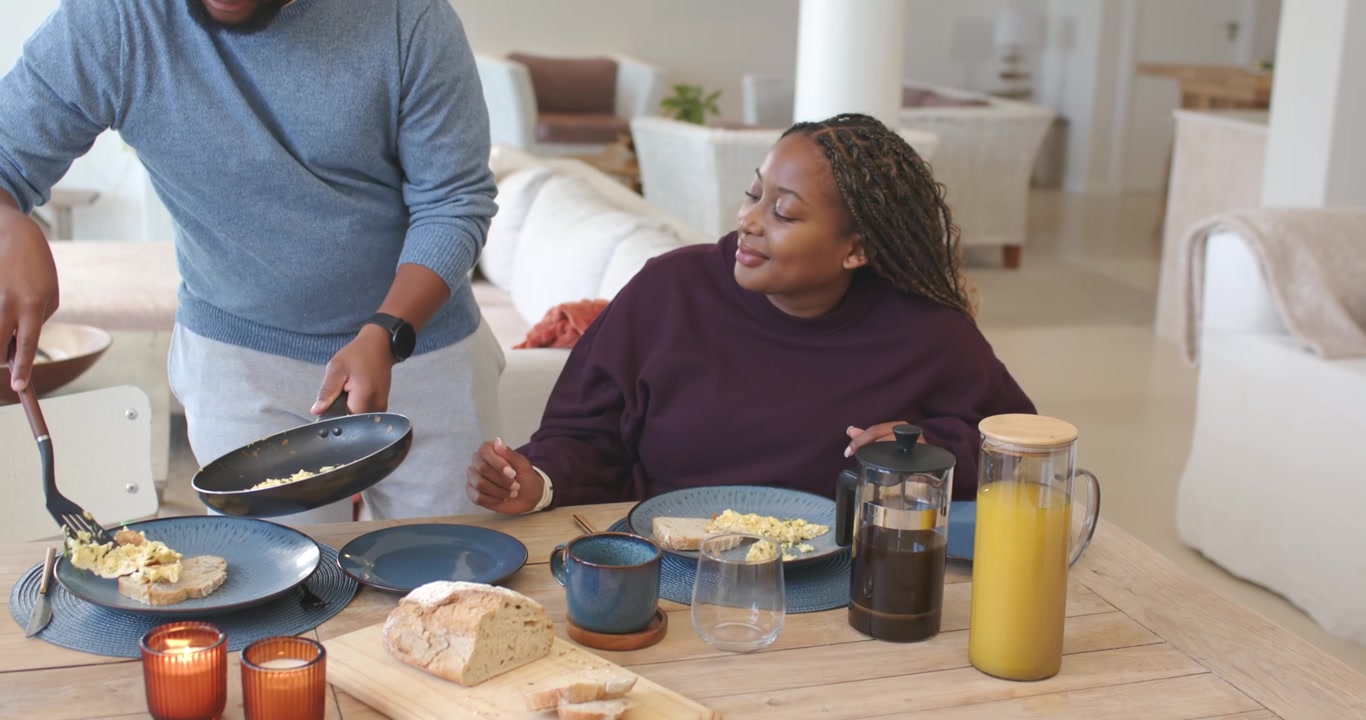 African American couple at table making breakfast man scooping eggs from pan woman holding press