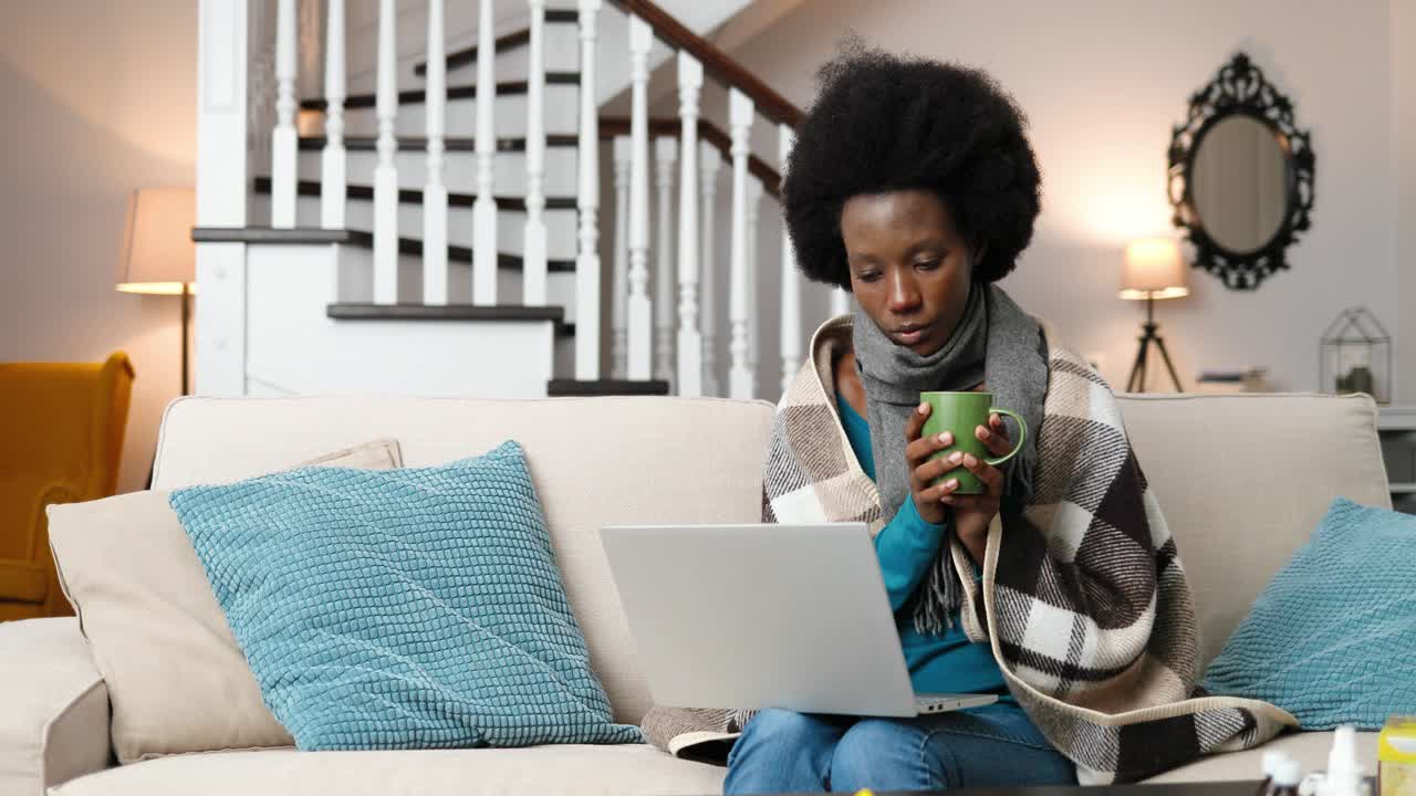 Sick woman looking at laptop screen and drinking tea in room