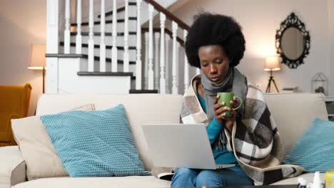 sick woman looking at laptop screen and drinking tea in room