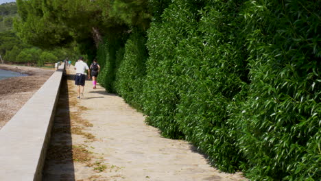 A-female-runner-catching-up-with-a-man-talking-in-the-phone-on-a-promenade-with-the-sea-to-the-left-and-trees-to-the-right