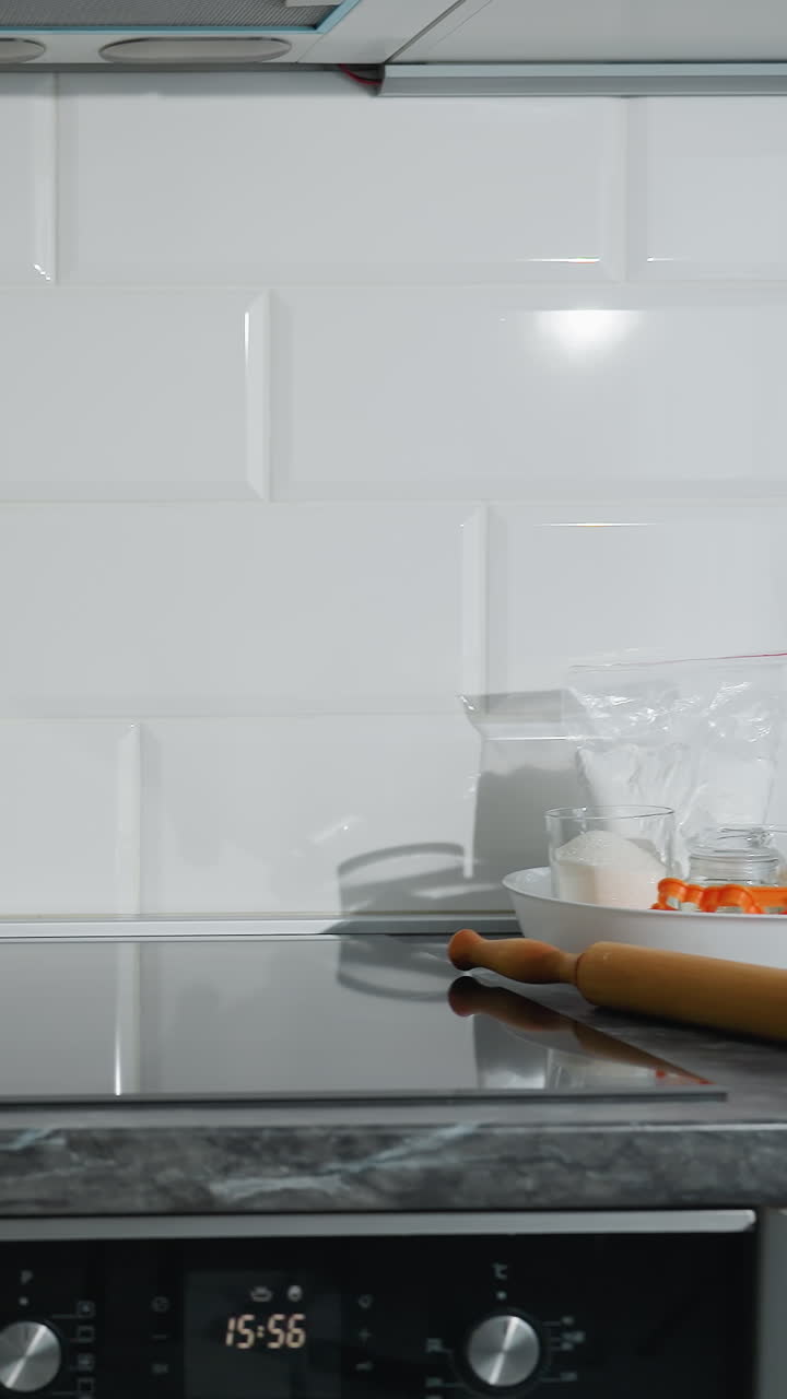 Linda cozinha moderna com elegante bancada de mármore preto, armários brancos e forno embutido. Utensílios de cozinha, rolo de massa, chaleira de vidro e ingredientes para assar bem organizados na área de trabalho