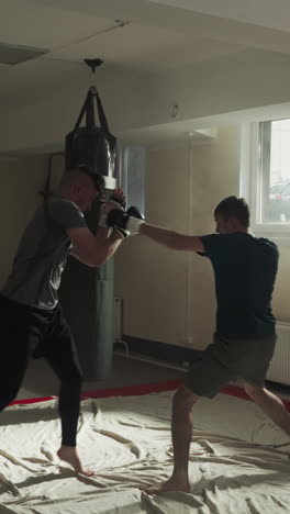 los kickboxers luchan en sparring amistoso en un club deportivo. los jóvenes maestros de artes marciales ejercitan ataques y bloques en un gimnasio vacío. los deportistas entrenan en combate.