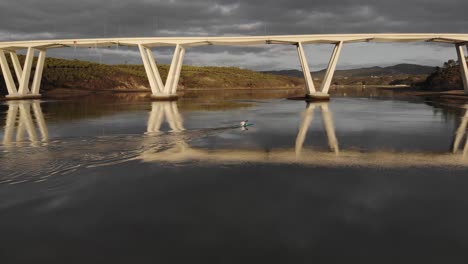 Single-canoeist-paddling-on-smooth-river-with-bridge-reflection