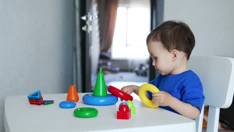 beautiful caucasian toddler sits at the desk. cute child plays with colorful toy pyramid.