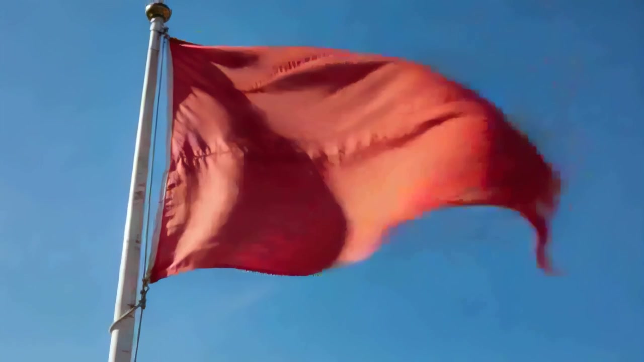 Bandera roja ondeando agitada por el viento racheado, cambiando de abultada a plana bajo un cielo azul claro, mástil
