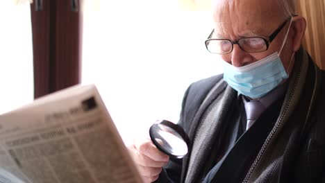 Senior man reading newspaper with magnifying glass while wearing face mask