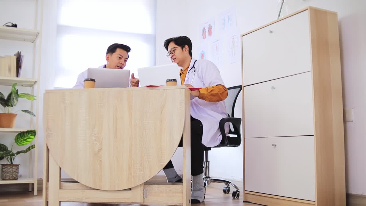 Two doctors collaborate discussing patient care using laptops in modern clinic office setting