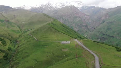 drone aerial view in georgia flying over gergeti trinity orthodox church in kazbegi surrounded by green mountains valley with snowed peaks