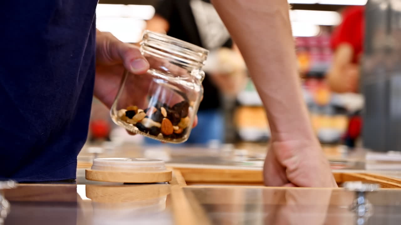 Man's hands filling a glass jar with nuts, dried fruits and berries in supermarket. Ecology idea. Side view