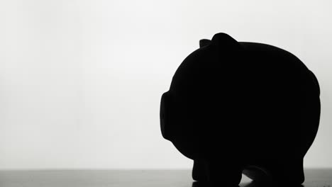 silhouette of a hand that throws coins into a piggy bank. on a white background