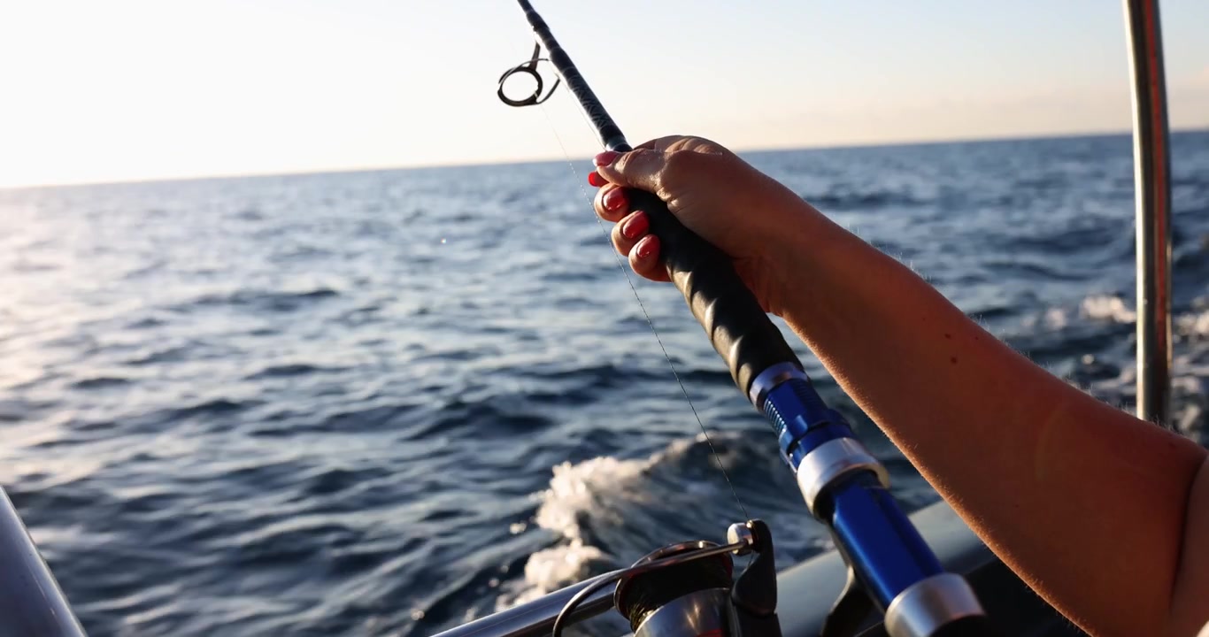 Žena drží rybářský prut na rychle jedoucí lodi na otevřeném oceánu.