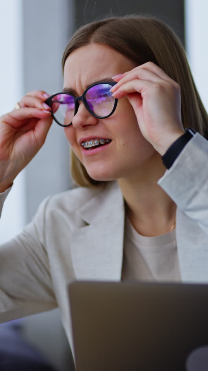 Cheerful lady sits with laptop in front of her. Woman is interested in something aside and puts on the glasses to see it better. Vertical video