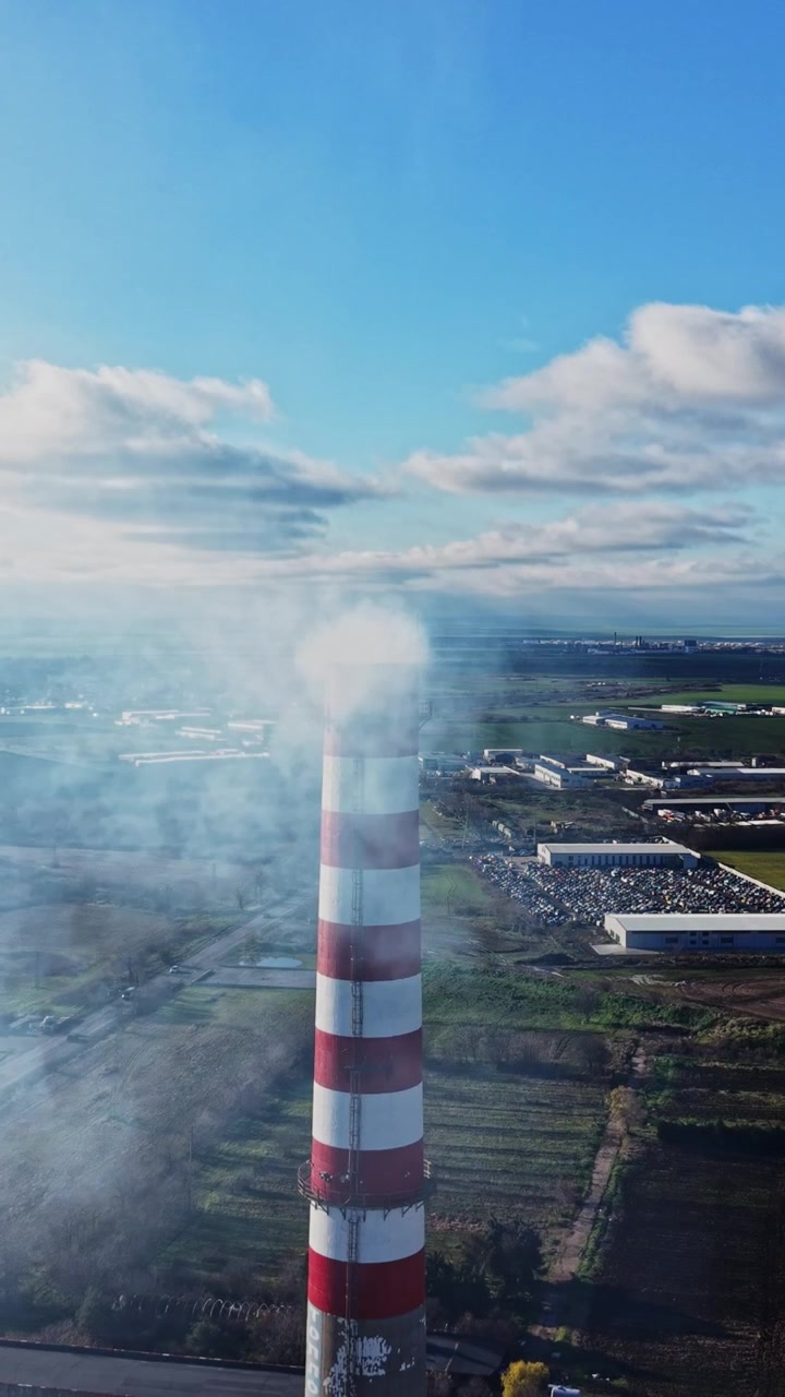 Industria e fumo che si alza da un'alta ciminiera in un paesaggio aperto
