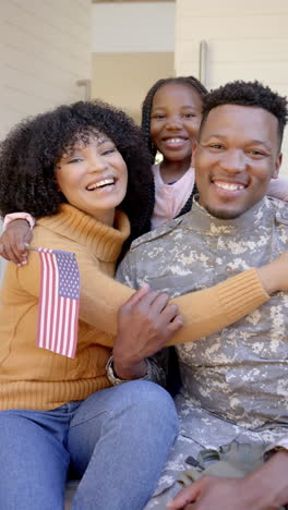 vertical video of portrait of happy african american male soldier with family at home, slow motion