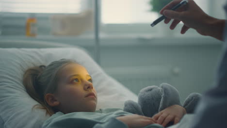 Physician-examining-little-patient-with-flashlight-test-in-hospital-closeup.