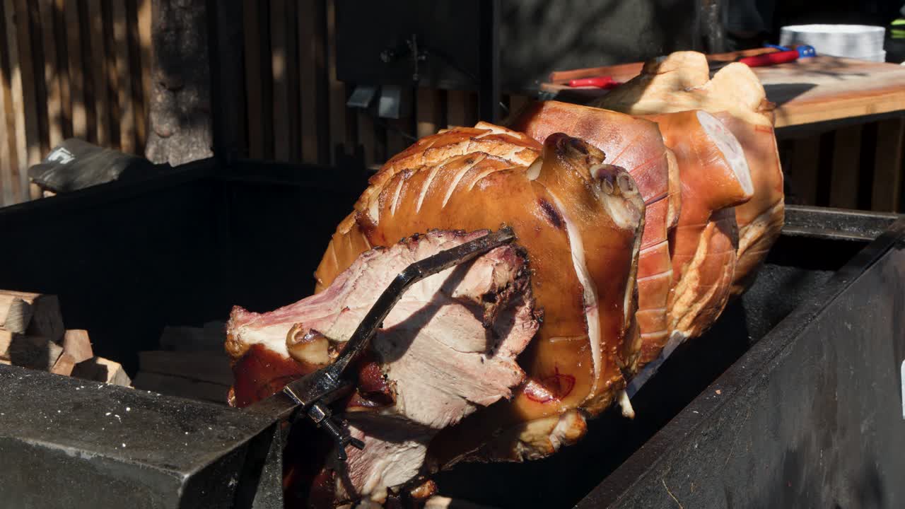 Whole pork slowly roasting on spit over open flame, outdoor market, natural sunlight, close-up view