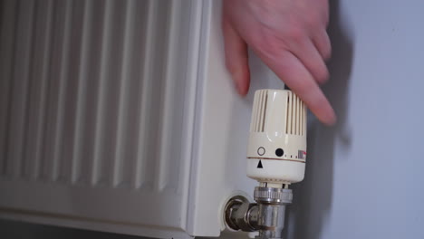 person turns down the heat from the radiator to cool down the house