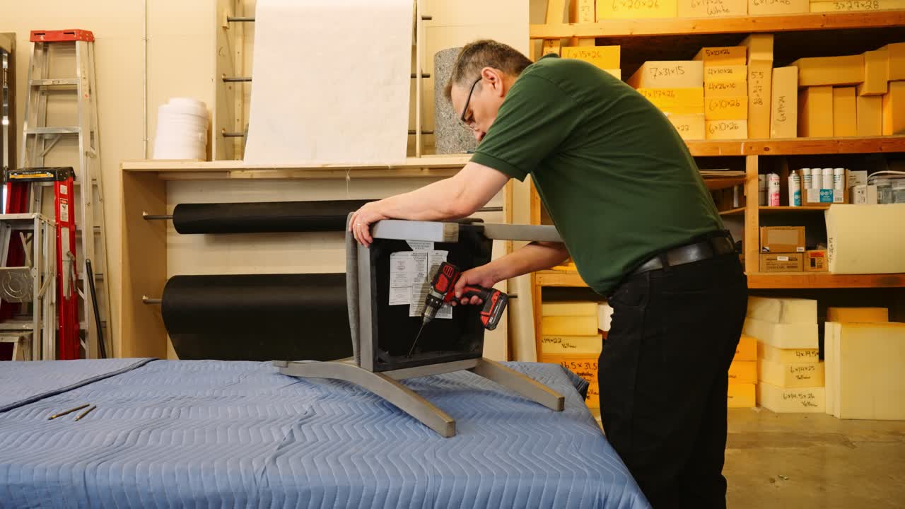 An older man furniture repair technician levels a dining chair inside a furniture repair shop