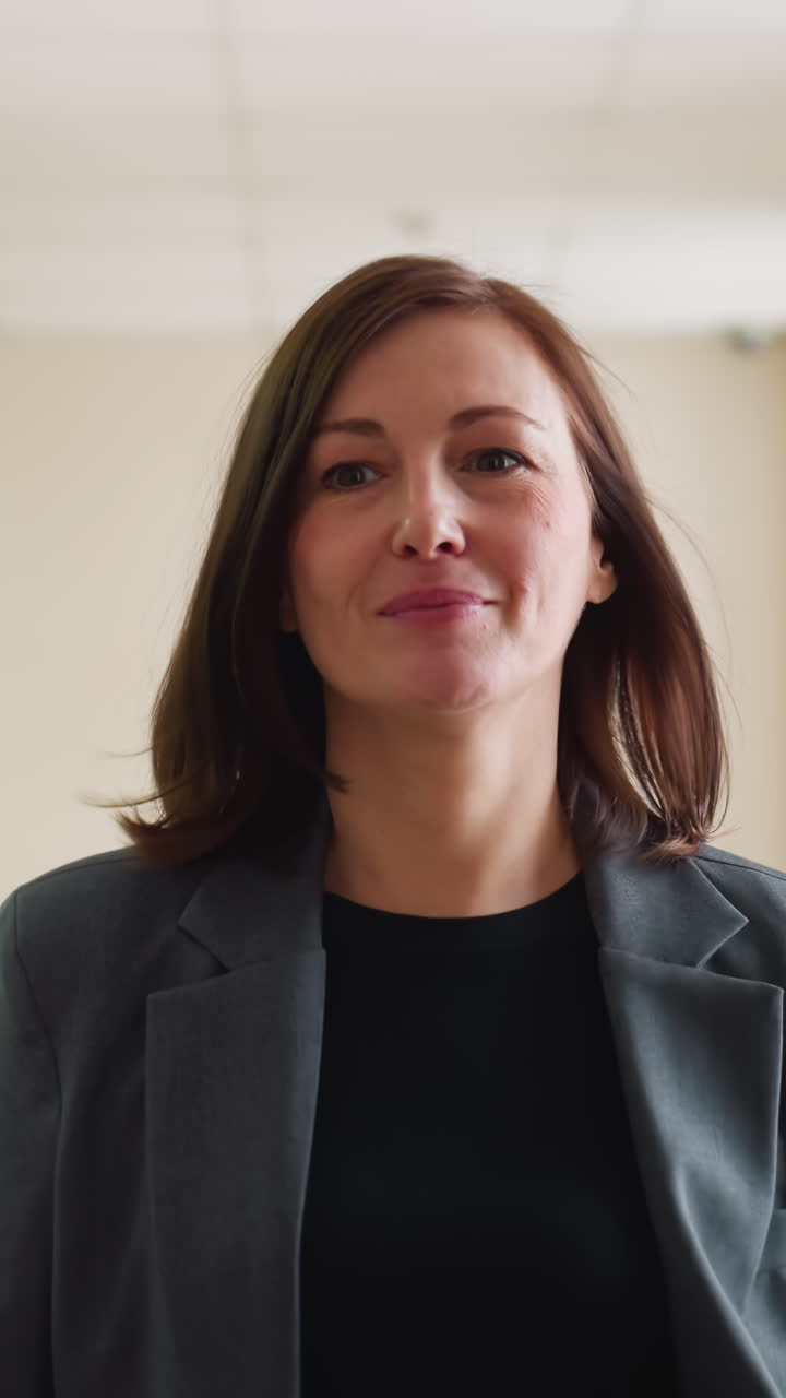 Donna d'affari sicura di sé in tailleur grigio che cammina nel corridoio dell'ufficio con una cartella rossa in mano e un sorriso dolce, pronta per una riunione o una presentazione, che mostra professionalità ed eleganza aziendale