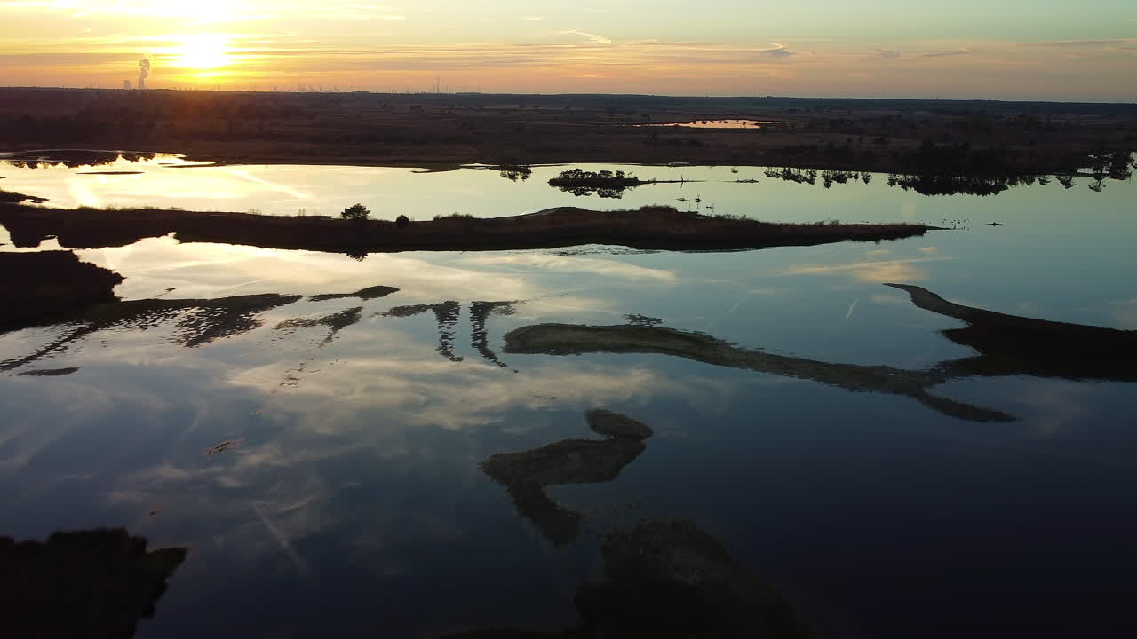 Filmisk solnedgang spejlende sig i sumpens vand, set fra drone