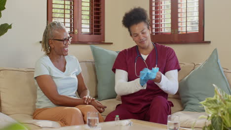preparing medical supplies, caregiver in scrubs with elderly woman smiling nearby, at home