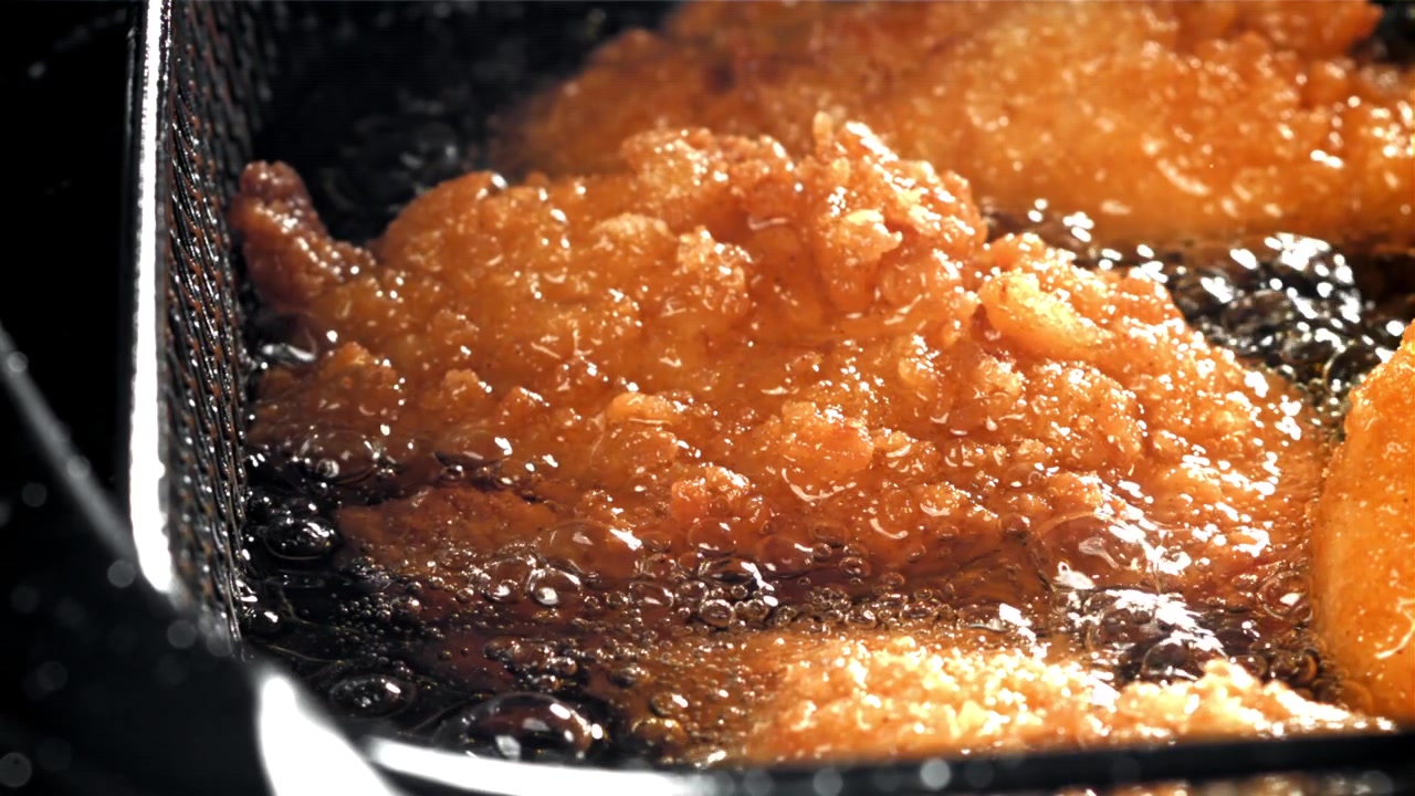 熱い油で揚がるきつね色のフライドチキンのクローズアップ