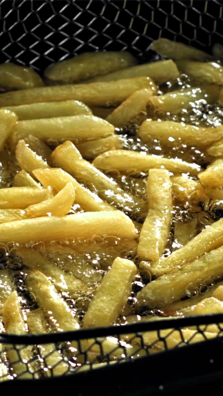 Primo piano di patatine fritte dorate che friggono nell'olio bollente