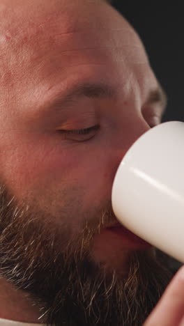 hombre barbudo toma cápsula prescrita bebiendo con agua de taza blanca. hombre con enfermedad cardíaca toma suplemento dietético para mejorar la condición de salud de cerca