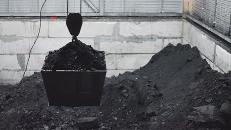 bucket with charcoal hangs on crane hoist over storage pool