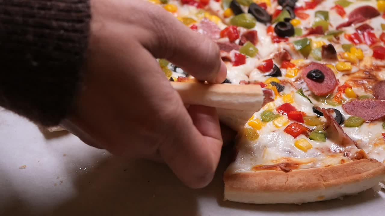 Primo piano di una mano che prende una fetta da una pizza appena sfornata