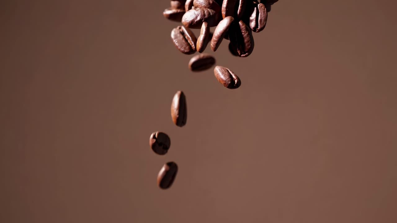 Video ravvicinato di chicchi di caffè che cadono su uno sfondo marrone