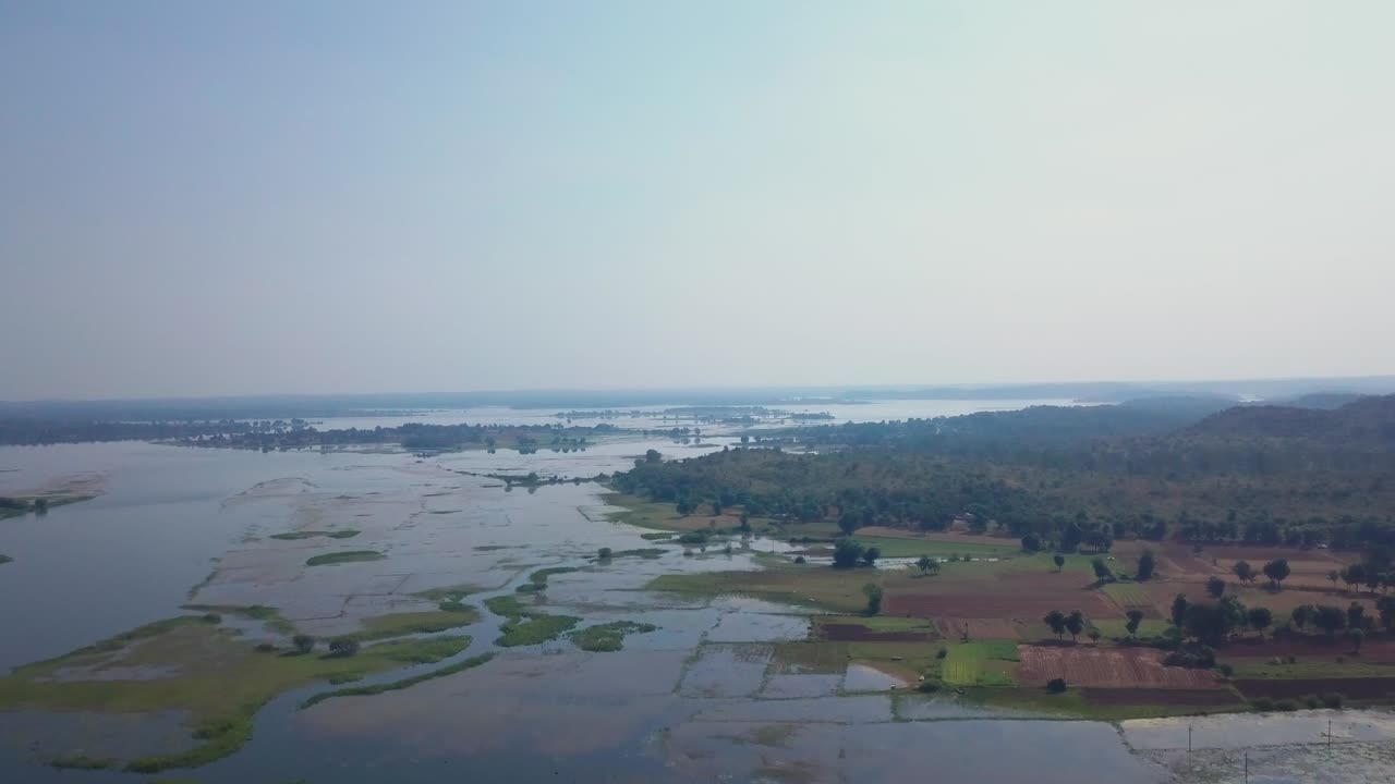 Campi agricoli allagati e zone umide si estendono nel paesaggio del Gujarat, India, dopo le piogge monsoniche. Una vista aerea rivela terreni agricoli inondati, vegetazione sparsa e canali d'acqua.