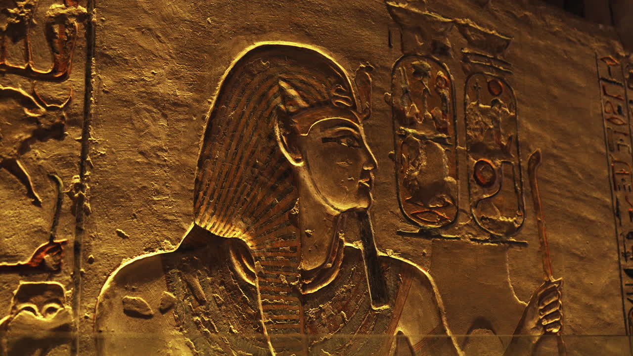 Carved wall relief showing an Egyptian figure with a long beard and tall headdress, surrounded by hieroglyphs. Ancient Egyptian art and symbolism preserved in stone
