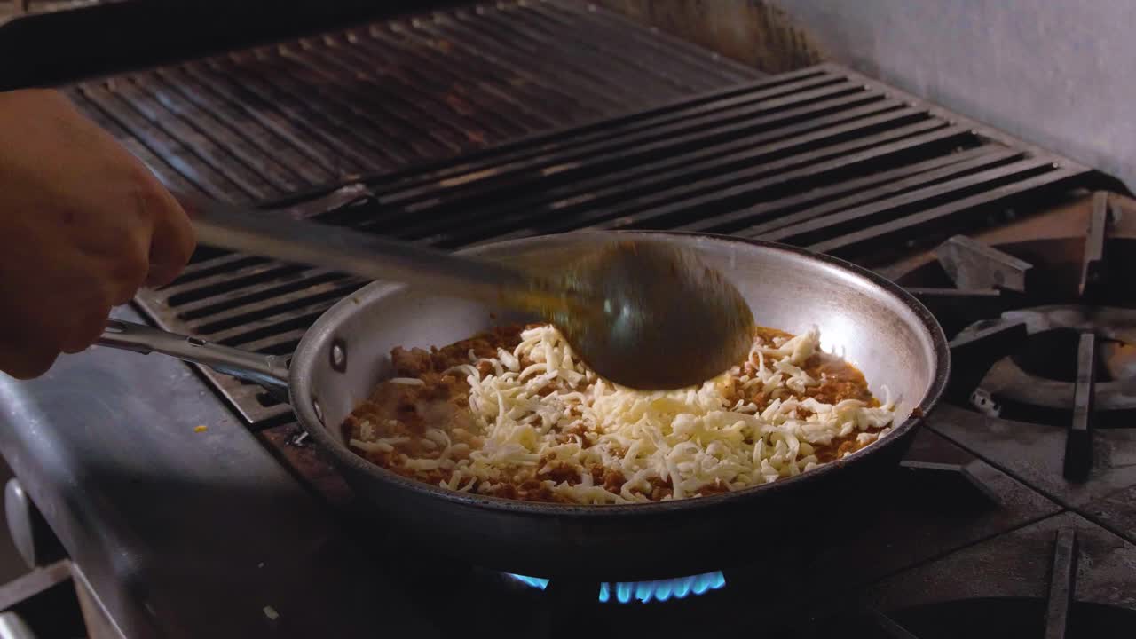 Mano che versa formaggio grattugiato in padella con salsa