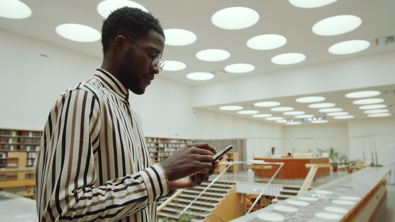 African American Man Surfing the Internet on Phone in Library