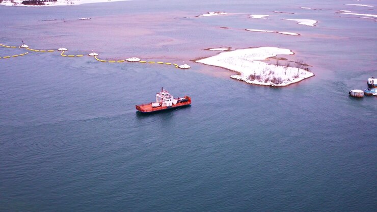 Drone view of a ferry crossing icy waters surrounded by snow-covered terrain.