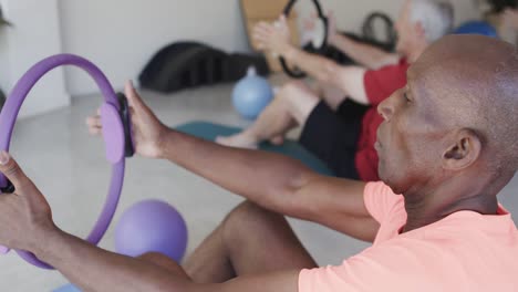 focused diverse seniors holding rings exercising in pilates class, unaltered, in slow motion