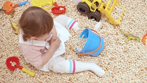 niña de 2 años arroja arena de playa como si fuera un cubo de juguete en un café infantil