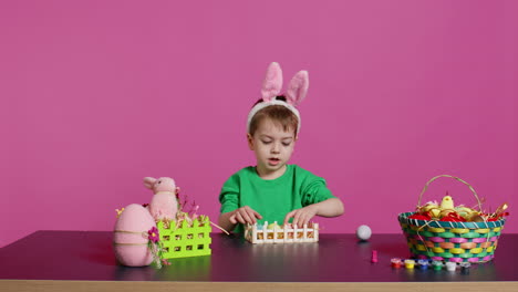 happy toddler with bunny ears arranging basket filled with painted eggs