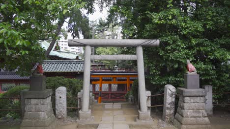 typical japanese stone torii gate with backdrop of red japanese temple - frontal view