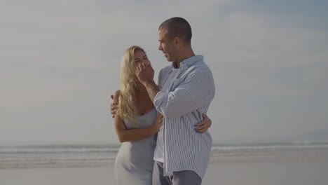 Happy-Caucasian-couple-walking-along-beach-hugging-and-smiling.