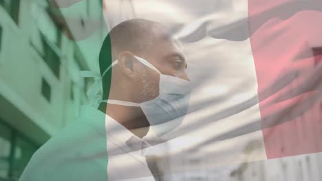 animation of flag of italy waving over man wearing face mask during covid 19 pandemic