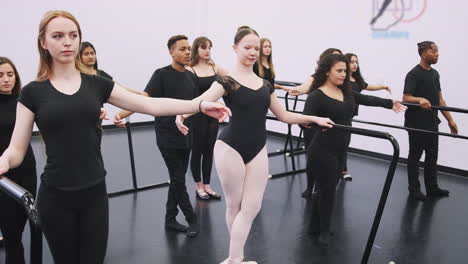 male and female students at performing arts school rehearsing ballet in dance studio using barre