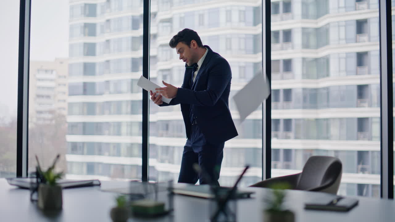 Nervous boss quarrelling smartphone throwing papers by office panoramic window
