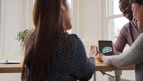 Business-woman-using-tablet-app-showing-3d-printed-model-of-geodesic-dome-walking-through-modern-office-to-diverse-team-meeting