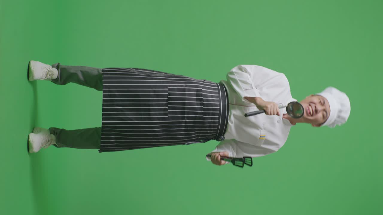 Full Body Of Asian Man Chef Holding Tongs And Ladle And Singing While Standing In The Green Screen Background Studio
