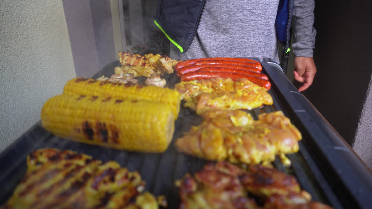 el hombre voltea la carne de pollo en la parrilla eléctrica con unas pinzas de silicona para alimentos