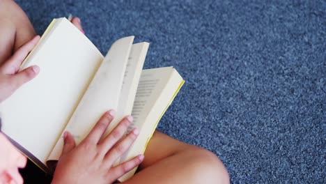 schoolgirl sitting on floor and reading a book in library at school