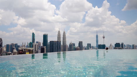 woman swimming in infinity pool on hotel rooftop with view of kuala lumpur city skyline in daytime