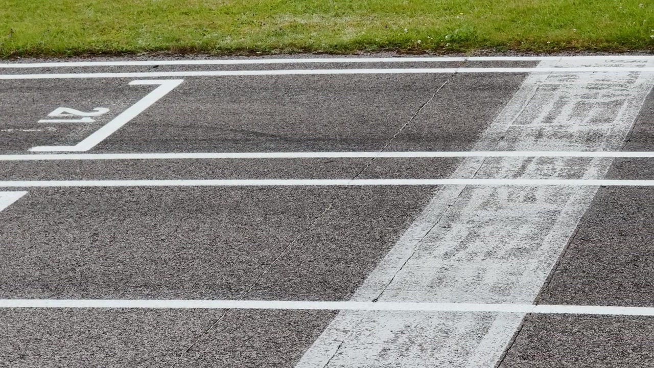Vista ravvicinata di corsie numerate in asfalto con segnaletica bianca nitida accanto all'erba verde, che mostra una superficie di pista sportiva pulita preparata per gare o allenamenti.